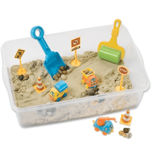 sensory bin with kinetic sand, construction vehicles, road signs, and a roller and shovel